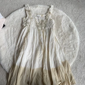 Vit och beige klänning från Miel (S) - Romantisk långklänning från Miel i vitt och beige med broderade blommor upptill och breda axelband. Klänningen har en luftig passform, perfekt för varma dagar.