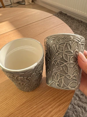 Mateus muggar  - Säljer två snygga keramikmuggar i grått med upphöjt bladmönster runt om. Insidan är vit och slät medan utsidan har en matt, strukturerad yta. Perfekta för te eller kaffe och ger en stilren känsla till köket. Från Mateus. Nypris: 400 kr.