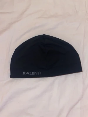 Svart sportmössa från Kalenji - En svart, tunn och stretchig sportmössa från Kalenji. Perfekt för löpning eller träning, med diskret logga framtill. Tillverkad i ett lätt och snabbtorkande material som sitter tajt på huvudet.