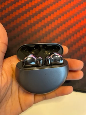 Huawei trådlösa in-ear hörlurar - Snygga trådlösa in-ear hörlurar från Huawei i metallicgrå färg. Hörlurarna kommer i ett runt, kompakt laddningsetui med Huawei-logga. Designen är modern och stilren med blanka ytor och ergonomisk passform. Perfekt för musik, poddar och samtal.