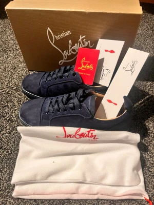 Mörkblå sneakers från Louboutin - Snygga mörkblå sneakers från Christian Louboutin i mocka med klassisk röd sula och blå snören. Skorna har en stilren design med lågt skaft och diskreta detaljer. Kommer med originalkartong, dustbag och äkthetskort. Pris ej hugget i sten!!!