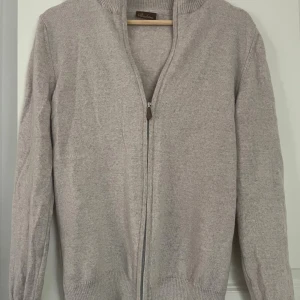 Beige hel-zip från Stenströms - Säljer en stilren beige helzip från Stenströms med dragkedja framtill. Koftan har långa ärmar och ribbade muddar vid ärmslut och nederkant. Perfekt för en avslappnad och elegant look. Perfekt för våren och ass snygg. Det står L men passar perfekt S. OBS modellen är 181cm och 63kg.