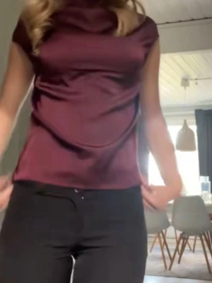 Vinröd satintopp med kort ärm - Snygg vinröd topp i glansigt satintyg med korta ärmar och lös passform. Toppen har en högre, draperad halsringning som ger en elegant look. Perfekt att styla med smycken för en trendig outfit.