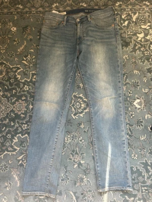 Ljusblå raka jeans från Levis - Ljusblå jeans med raka ben och klassisk femficksdesign från Levis. Jeansen har en lätt tvättad look med subtila slitningar på framsidan och normal midja. Perfekta för en avslappnad och trendig stil.