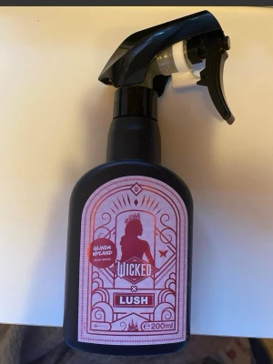 Lush Wicked Lush Glinda  Body Spray - Wicked Glinda Hyland body spray från Lush i en svart plastflaska med spraymunstycke. Flaskan har rosa etikett med siluettmotiv och rymmer 200 ml. Perfekt för dig som gillar unika och fräscha dofter.