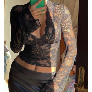 Svart spetsblus - Snygg svart spetsblus med djup v-ringning och långa ärmar. Perfekt för en kväll ute eller en speciell tillställning. Blusen har ett elegant och sofistikerat utseende med genomskinliga detaljer.