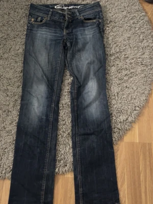 Mörkblå bootcut jeans från Esprit - Säljer ett par mörkblå bootcut jeans från Esprit med snygga slitningar och kontrastsömmar. Klassisk femficksmodell med knappgylf och låg midja. Perfekta för dig som gillar en avslappnad men ändå trendig look.