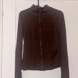 Brun ziptröja med hög krage - Snygg brun ziptröja med hög krage och långa ärmar. Tröjan har en slimmad passform och dragkedja framtill. Perfekt att slänga på sig över en t-shirt. Materialet känns mjukt och stretchigt.