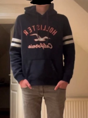 Hollister hoodie - hoodien är marin blå bara dåligt ljus skriv privat om ni vill ha mer bilder. Tröjan har sånt fodrigt typ av material på insidan som är super bekvämt. Modellen är 179cm och väger 69. Skick 9/10 en pytte liten lös tråd/hål, se sista bilden, men annars helt fel fri skriv om ni har några frågor!
