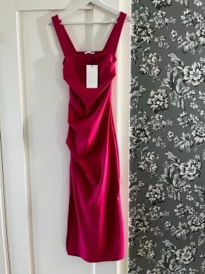 Zara ceriserosa klänning i storlek S - Snygg ceriserosa klänning från Zara med breda axelband och figurnära passform. Klänningen har draperade detaljer framtill och är tillverkad i ett mjukt, stretchigt material. Perfekt för dig som vill sticka ut. Ny med prislapp