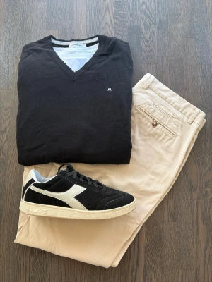 Stickad V-ringad tröja J.Lindeberg - Klassisk svart V-ringad tröja från J.Lindeberg med diskret logga på bröstet. Tröjan har normal passform och är stickad, perfekt att bära över en t-shirt eller skjorta. Tröjan är i väldigt fint skick och passar till nästan alla outfits.