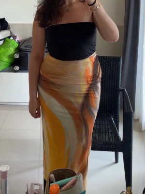 Midikjol med  mönster i orange/brun/beige/gult  - Säljer en midikjol med abstrakt mönster i orange, gult, vitt och brunt. Kjolen har en figurnära passform och är gjord i ett mjukt, stretchigt material som sitter snyggt på kroppen. Perfekt för dig som vill sticka ut med färg och form. Nypris: 359kr. ❤️