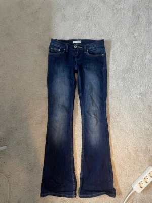 Mörkblå bootcut jeans från Replay - Snygga mörkblå bootcut jeans från Replay med klassisk femficksmodell och dekorativa sömmar på bakfickorna. Jeansen har låg midja och är tillverkade i slitstark denim med lätt tvättade detaljer. Perfekta för en avslappnad och trendig look.