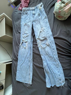 Ljusa slitna jeans från FB Sister - Säljer ett par ljusblå jeans från FB Sister i storlek L. Jeansen har vida ben, råa kanter nertill och stora slitningar på båda benen för en riktigt trendig och avslappnad look. Perfekta för dig som gillar streetstyle och oversized passform.