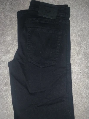 Svarta slim jeans från Jack & Jones - Snygga svarta jeans från Jack & Jones i modellen Slim/Glenn. Jeansen har en smal passform och klassisk femficksdesign. Perfekta för dig som gillar en stilren och enkel look. Materialet är mjukt och stretchigt för extra komfort.