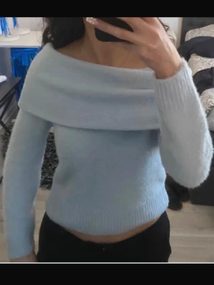 Stickad tröja  - Säljer en supermjuk och fluffig ljusblå stickad tröja med offshoulder-design och långa ärmar. Tröjan har en bred krage som vilar över axlarna och är croppad i modellen. Perfekt för dig som vill ha en trendig och mysig look. Passar s också