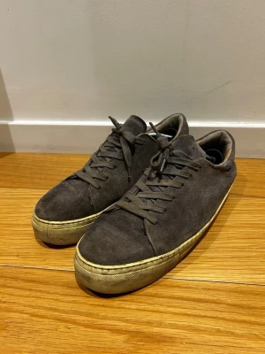 Rizzo Sneakers *43* - Stilrena sneakers i brun mocka med klassisk låg profil och beige sula. Skorna har rund tå, matchande bruna skosnören och en enkel design som passar till det mesta. Perfekta för dig som gillar en clean och tidlös look.