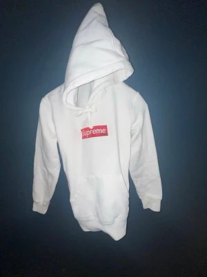 Vit Supreme hoodie - Hoodie från Supreme i vitt med den klassiska röda box loggan på bröstet. Mjuk insida och stor huva, samt magficka framtill. Perfekt för dig som vill ha en clean streetwear-look. Extra tjockt tåligt material. Det stl Medium på lappen men den är som en Small. 