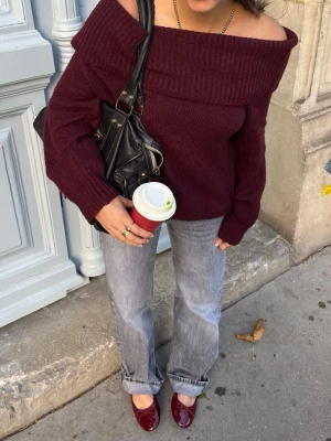 Vinröd off shoulder stickad tröja - Snygg vinröd stickad tröja med bred off shoulder-krage. Tröjan har en avslappnad passform och långa ärmar, perfekt för lager-på-lager. Passar dig som gillar trendiga och bekväma plagg med lite extra attityd.