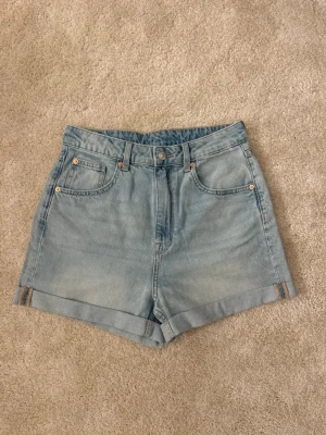 Ljusblåa högmidjade jeansshorts - Snygga ljusblåa jeansshorts med hög midja och klassisk femficksdesign. Shortsen har uppvikta benslut och bälteshällor.