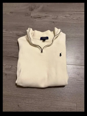Vit halvzip-tröja från Polo Ralph Lauren - Snygg vit tröja med halv dragkedja från Polo Ralph Lauren. Klassisk design med broderad logga på bröstet och ståkrage. Perfekt för en clean och stilren look. Passform xs-s