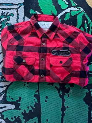 Röd och svart rutig skjorta Levi's - Klassisk röd och svart rutig skjorta från Levi's med två bröstfickor och knappar framtill. Skjortan har lång ärm och en patch med Levi Strauss & Co. på bröstet. Perfekt för en avslappnad och cool stil.