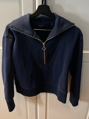 Mörkblå hoodie med dragkedja från GANT - Snygg mörkblå hoodie från GANT med bred krage och silverfärgad dragkedja framtill. Perfekt för en avslappnad och stilren look.