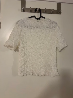 Vit blus med 3D-blommönster - Superfin vit blus med kort ärm och unikt 3D-blommönster över hela tyget. Blusen är lätt transparent och är perfekt till sommaren. Den är aldrig använd och i storlek M, men passar även S.