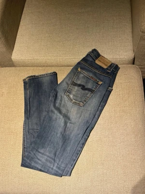 Blå jeans från Nudie Jeans - Snygga blå jeans från Nudie Jeans . Jeansen har en något tvättad look och är tillverkade i denim. Perfekta för en avslappnad stil. Hål på höger knä se bild 3. Skriv vid funderingar!!!