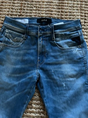 Blå jeans från Replay, midja 28/32 - Snygga blå jeans från Replay med klassisk femficksdesign och lätt slitna detaljer. Jeansen har normal midja och raka ben. Tillverkade i bomull med en skön stretch för extra komfort. Perfekta för en avslappnad och trendig look.