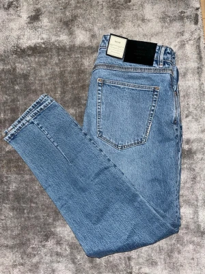 Blå raka jeans från Neuw - Säljer ett par klassiska blå jeans från Neuw med rak passform och hög midja. Jeansen är tillverkade i stretchig ring-spun bomullsdenim och har en autentisk indigo tvätt. Perfekta för en avslappnad och trendig look.