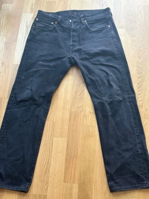  Levi's jeans 501 w32 L30 - Säljer ett par svarta jeans från Levi's med klassisk femficksdesign och raka ben. Jeansen har en enkel look med nitar vid fickorna och Levi's ikoniska läderpatch bak i midjan. Perfekta för en clean och stilren outfit.