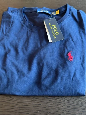 Marinblå t-shirt från Polo Ralph Lauren - Snygg marinblå t-shirt från Polo Ralph Lauren med klassisk röd broderad logga på bröstet. Tillverkad i mjuk bomull och har en normal passform med korta ärmar. Perfekt basplagg för en clean och stilren look.