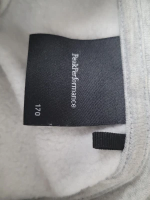 Grå hoodie från Peak Performance - Snygg ljusgrå hoodie från Peak Performance i mjukt bomullsmaterial. Klassisk modell med långa ärmar, ribbade muddar och huva. Perfekt för chill dagar eller när du vill ha en clean och enkel stil. Använd 1 gång