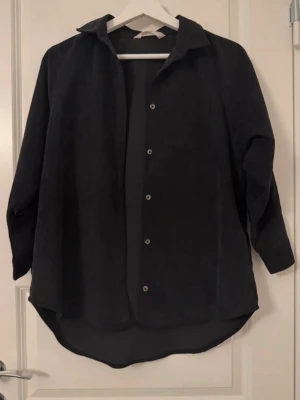 Svart overshirt i manchester - Stilren svart overshirt i mjuk manchester med klassisk krage och knappar framtill. 