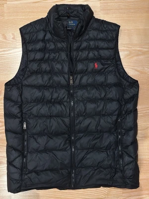 Ralph Lauren väst - Snygg svart dunväst från Polo Ralph Lauren med dragkedja och röd broderad logga på bröstet. Väldigt fin väst inga skador. Nypris : 3659 kr   Skriv för mer info. 