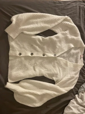 Vit kofta från Nelly med knappar - Mysig vit kofta från Nelly i ribbstickat material. Koftan har långa ärmar och knappar. Den har en fläck som inte är så jätte synlig som troligtvis går bort i tvätten. Den är bara använd 1-3 gånger.