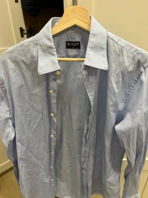 Tiger of Sweden skjorta - Säljer en ljusblå skjorta från Tiger of Sweden i slim fit. Skjortan har klassisk krage, vita knappar och långa ärmar. 