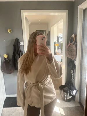 Beige kappa med knytskärp - Stilren beige kappa med knytskärp i midjan. Suuuper snygg samt att matrialet liknar Arket jackorna. 