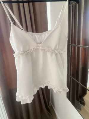 Vit volang linnetopp med smala band - Supersöt vit linnetopp med smala axelband och volangdetaljer, perfekt till vår/ sommar!