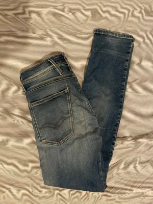 Blå slim fit jeans från Replay - Säljer ett par blå slim fit jeans från Replay med snygga slitningar och klassiska fem fickor. Jeansen har en något tvättad look och smala ben. Perfekta för dig som gillar en modern och avslappnad stil W28 L30 replay anbass hyperfelx