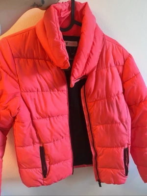 Röd pufferjacka från H&M - Snygg röd pufferjacka från H&M med hög krage och två dragkedjeförsedda fickor framtill. Jackan har quiltad design och kortare passform, perfekt för kalla vinterdagar. Tillverkad i syntetmaterial som håller värmen och ger en cool look.