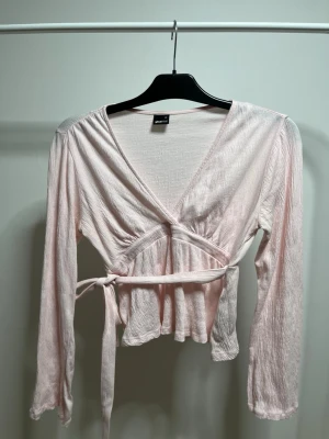 Ljusrosa topp med knyte i ryggen från Ginatricot - Rosa topp från Gina tricot med knyte i ryggen och en v ringning, den är väldigt skrynklig för jag inte använt den på väldigt länge, sndvänt 3 gånger