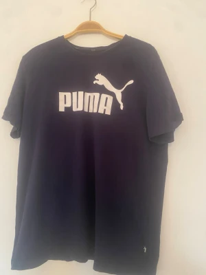 Mörkblå Puma t-shirt med logga - Snygg mörkblå t-shirt från Puma med stor vit logga och text på bröstet. Klassisk rund hals och korta ärmar. Perfekt för en sportig och avslappnad stil.