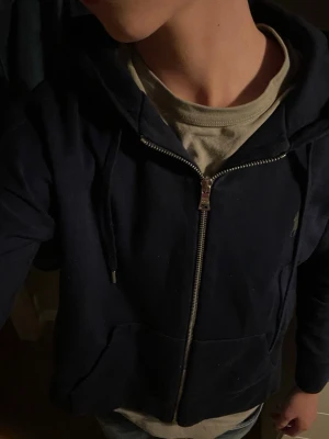 Mörkblå hoodie från Ralph Lauren - Snygg mörkblå hoodie från Ralph Lauren med dragkedja framtill och klassisk huva. Tröjan har det ikoniska Polo-logotrycket på bröstet och ribbade muddar vid ärmar och nederkant. Perfekt för en avslappnad och stilren look. Skick 9/10 Inga defekter, storlek XS kom om du har minsta lilla fråga! 🔥📦