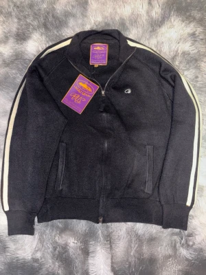 Svart zip hoodie från Corteiz med sopiga stripes - Svart hoodie från Corteiz med vita stripes längs ärmarna och stor broderad logga på ryg fitness-vibe. Dragkedja framtill, två fickor och liten broderad logga på bröstet. Har inte använt den helt ny. Passar för dig som har mellan S/M i storleken 