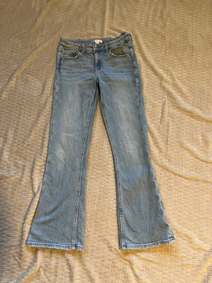 Ljusblå bootcut jeans - Säljer ett par ljusblå bootcut jeans med klassisk femficksdesign och normal midja. Jeansen har en lätt utsvängd passform nedtill och sitter lite löst upptill. Har en sliten look vid midjan, fickorna och längst ner på benen. Har ställbar midja. Material: 99% bomull, 1% elastan.