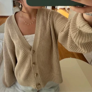 Beige oversized kofta med knappar - Mysig beige kofta i oversized modell med stora knappar framtill. Stickad i grovt garn och har långa ärmar med breda muddar. Perfekt att slänga över ett linne eller t-shirt för en chill look.