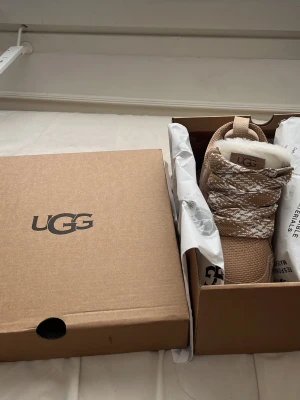 Beige sneakers från UGG med pälsfoder - Orginal pris 1950kr. Snygga beige sneakers från UGG med grov sula och pälsfoder. Skorna har stickade och mockadetaljer, samt mönstrade snören i vitt och beige. Perfekta för dig som vill ha både stil och komfort under kyligare dagar.