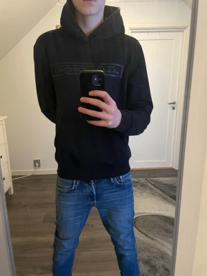 Svart hoodie från J.Lindeberg - Snygg svart hoodie från J.Lindeberg med stor logga på bröstet. Klassisk modell med huva och dragsko, samt ribbade muddar vid ärmslut och midja. Tillverkad i mjukt material som känns skönt mot huden. Perfekt för en avslappnad och stilren look. Storlek M och priset kan diskuteras 